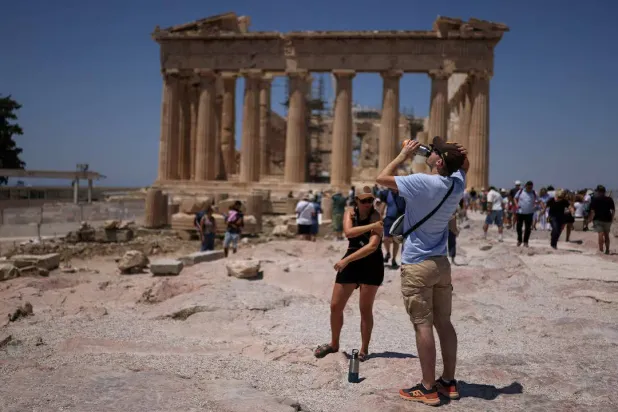 سائح يشرب الماء خلال زيارته لمعبد البارثينون في ظل موجة حرّ تضرب أثينا في اليونان يوم 27 يونيو 2025 (رويترز)