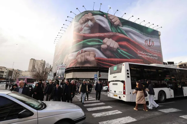 People walk past a large patriotic banner depicting the Iranian flag on Enghelab Square in Tehran on January 14, 2026.  (Photo by ATTA KENARE / AFP)