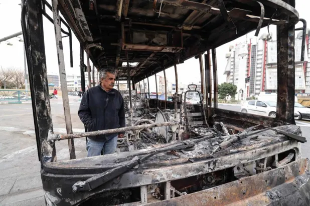 A man stands by the wreckage of a burnt bus bearing a banner (unseen) that reads "This was one of Tehran’s new buses that was paid for with the money of the people’s taxes,” in Tehran's Sadeghieh Square on January 15, 2026. (AFP)