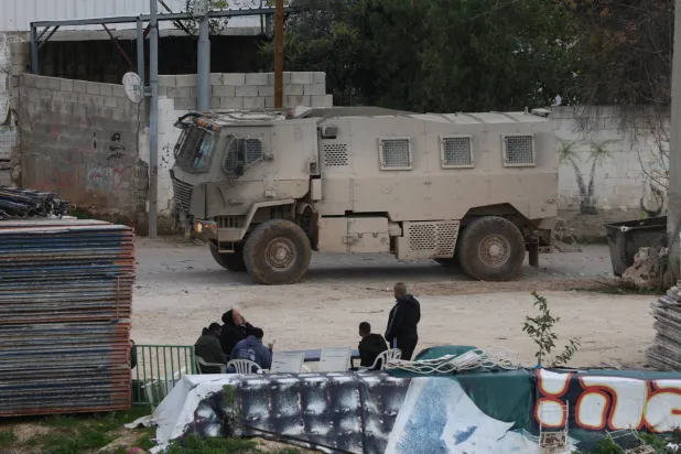 فلسطينيون يشاهدون آلية عسكرية إسرائيلية تنقل جنوداً إلى مخيم نور شمس قرب طولكرم بالضفة الغربية (إ.ب.أ)