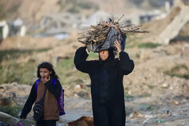 Filistinli bir kadın, Gazze Şeridi'nin merkezindeki Nuseyrat mülteci kampında ateş yakmak için odun taşıyor (AFP)