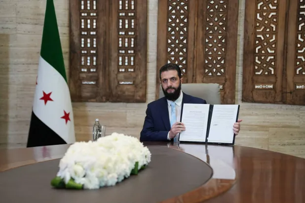 الرئيس السوري أحمد الشرع يرفع أمام الصحافيين اتفاقية وقف إطلاق النار والاندماج الكامل لـ«قسد» ضمن مؤسسات الدولة (أ.ف.ب)