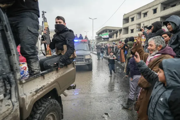 Yol kenarında sıralanarak, Rakka’daki Tabka ilçesine giren Suriye güvenlik güçlerine el sallayan Suriyeliler (EPA)