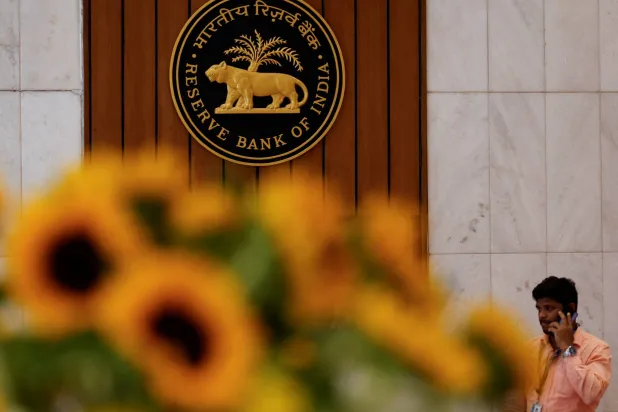 رجل يتحدث من هاتفه أثناء مروره بجانب شعار البنك الاحتياطي الهندي داخل مقرّه في مومباي (رويترز)