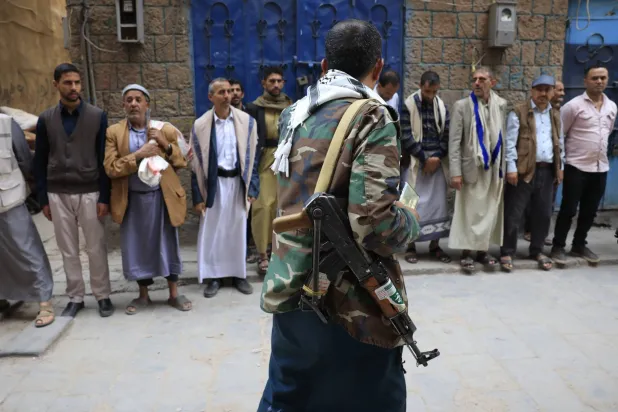 مسلّح حوثي يمر أمام تجمع للسكان بأحد أحياء صنعاء (إ.ب.أ)