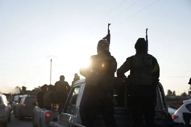 Syrian government forces brandish their weapons as they take possession of the SDF military base as they enter the city of Raqqa on January 19, 2026. (AFP)