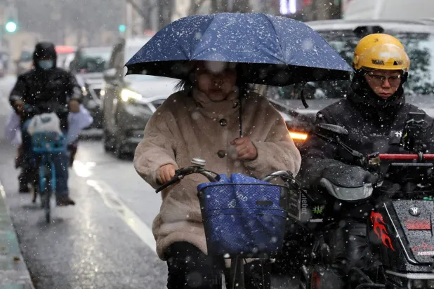 A woman holding an umbrella rides a bicycle amid snowfall in Shanghai, China January 20, 2026. (Reuters)