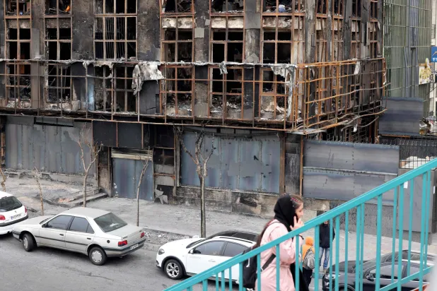 امرأة تمشي فوق جسر بجوار مبنى محترق دمر خلال الاحتجاجات العامة في طهران (أ.ف.ب)