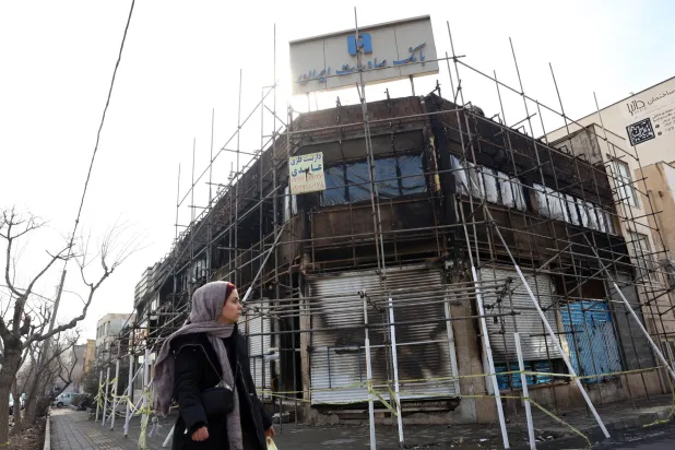 إيرانية تمر أمام فرع لبنك صادرات تضرر جراء حريق اندلع خلال الاحتجاجات (إ.ب.أ)