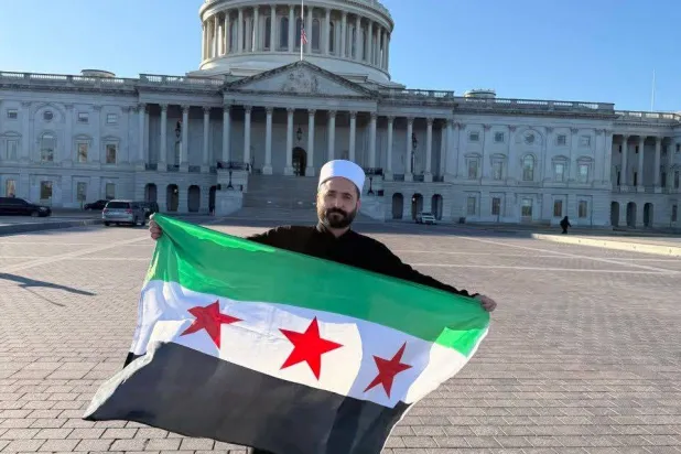 سليمان عبد الباقي مدير الأمن الداخلي في السويداء يرفع العلم السوري أمام مبنى الكونغرس في واشنطن (إكس)