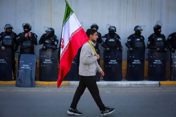 An Iraqi man carrying the Iranian flag passes in front of security forces outside the Iranian embassy in Baghdad during a demonstration to show solidarity against US threats (DPA). 