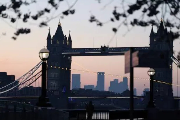 رجل يلتقط صوراً أثناء شروق الشمس خلف جسر البرج ومنطقة كاناري وارف المالية في لندن (رويترز)