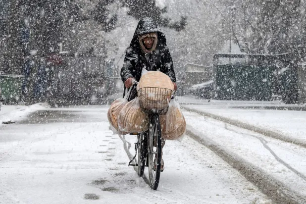 An Afghan man rides a bicycle along a road during snowfall in the green zone area of Kabul on January 22, 2026. (AFP)