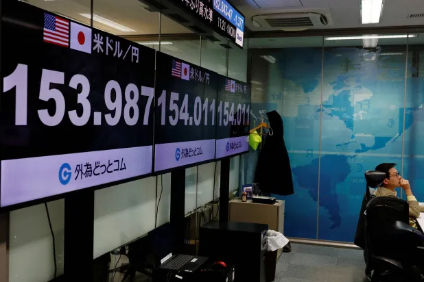 موظف في شركة لتداول العملات الأجنبية يعمل أمام شاشات تعرض سعر صرف الين الياباني مقابل الدولار الأميركي (رويترز)