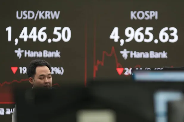 متداول يمرّ قرب شاشات تعرض مؤشر كوسبي وسعر صرف الدولار مقابل الوون في قاعة تداول بنك هانا بسيول (أ.ب)