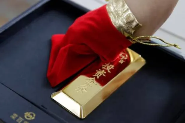 مساعد مبيعات يعرض سبيكة ذهبية في متجر كايباي للمجوهرات ببكين (رويترز)