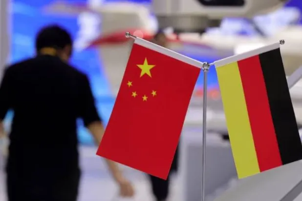 شخص يسير بجانب علمي الصين وألمانيا خلال الدورة الثامنة للمعرض الدولي الصيني للاستيراد في شنغهاي (رويترز)