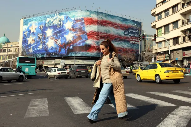 إيرانية تعبر ساحة «انقلاب» وسط طهران بالقرب من لافتة ضخمة مناهضة للولايات المتحدة (إ.ب.أ)