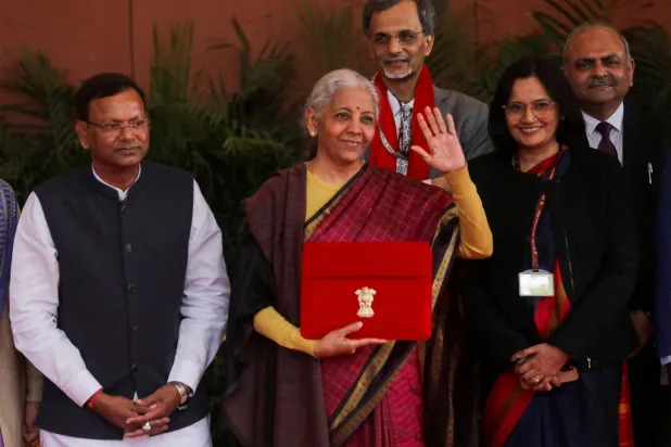 وزيرة المالية الهندية نيرمالا سيثارامان تلوّح بيدها وهي تحمل ملفاً عليه شعار الحكومة الهندية قبل مغادرة مكتبها لتقديم الموازنة الفيدرالية السنوية في البرلمان (رويترز)