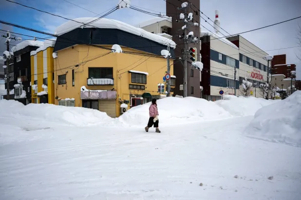 A pedestrian walks on the snow covered intersection in Aomori city, Aomori prefecture on January 30, 2026. (Photo by Philip FONG / AFP)