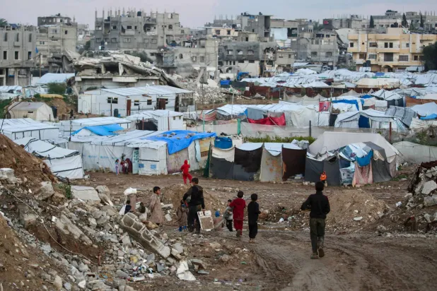 Children walk past tents and makeshift shelters in the Bureij refugee camp in the central Gaza Strip on February 3, 2026. (Photo by Eyad BABA / AFP)