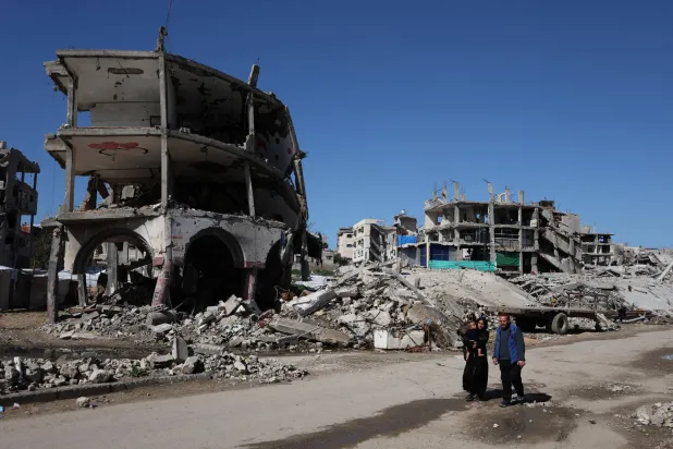 فلسطينيون يمرون أمام منازل بنايات مدمّرة بفعل الغارات الإسرائيلية في مدينة غزة أمس (رويترز)