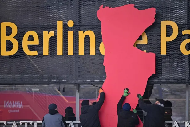 عمال يركّبون دبّ مهرجان برلين السينمائي الدولي على واجهة قصر برلين المقر الرئيسي للمهرجان استعداداً لانطلاق فعالياته (أ.ف.ب)