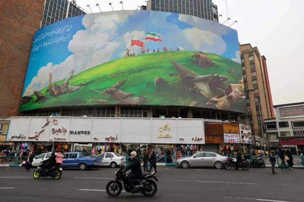 Tahran’daki bir meydanda bulunan binanın üzerinde yer alan ABD karşıtı afişin önünden geçen İranlılar