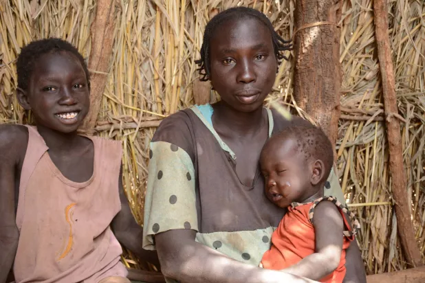 أم فرَّت مع طفليها من الحرب بالسودان تجلس في مخيم ثوبو (رويترز)