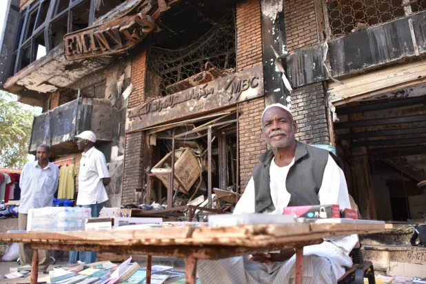 بائع سوداني أمام منزل تعرض للتدمير في العاصمة الخرطوم (د.ب.أ)