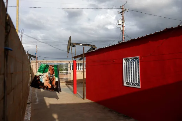 مضخة نفط خلف منزل سكني، حيث تتدلى بطانية بنقشة جلد النمر على سياج على ضفاف بحيرة ماراكايبو، فنزويلا (رويترز)