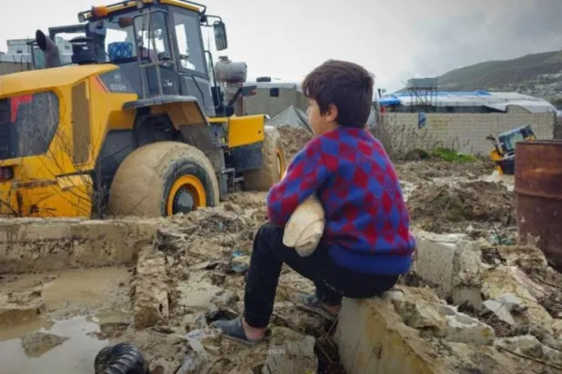 A child watches as civil defense teams open flooded roads in Idlib. (SANA) 