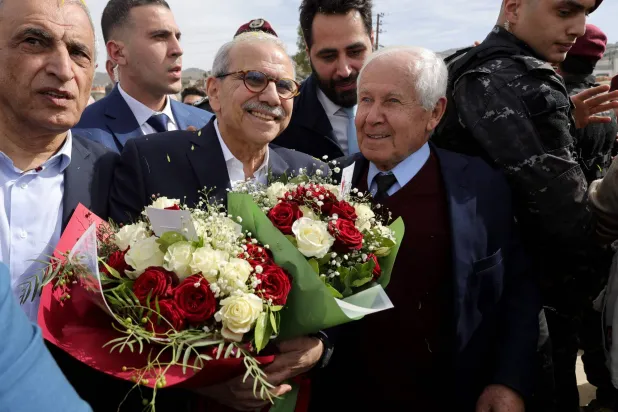 Lebanon's Prime Minister Nawaf Salam (L) holds bouquets of flower as he stands next to the mayor of the heavily-damaged southern village of Kfar Shouba, near the border with Israel, during his visit on February 8, 2026. (AFP)