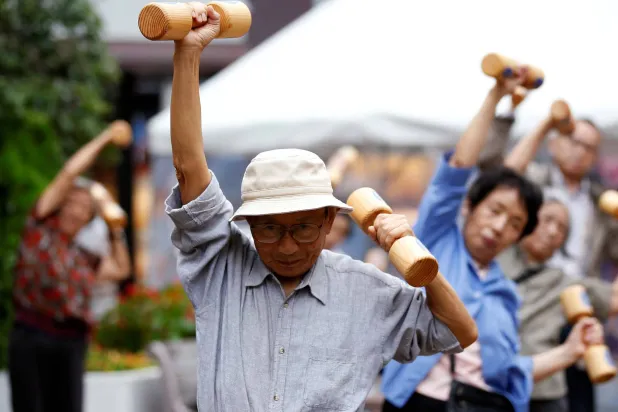 كبار السن ومتوسطو العمر يمارسون تمارين رياضية باستخدام أثقال خشبية خلال فعالية للتوعية الصحية في معبد بحي سوغامو بطوكيو (أرشيفية-رويترز)