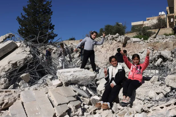 فتيات فلسطينيات يرفعن علامة النصر على أنقاض مبانٍ هدمتها إسرائيل في بيت عوا بمدينة الخليل بالضفة الغربية (أ.ف.ب)