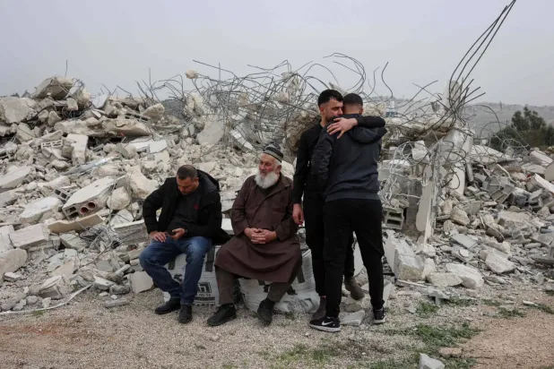 Ramallah'ın batısındaki Şukba köyünde dün İsrail tarafından yıkılan bir evin enkazı arasında oturan iki kişiyi teselli etmeye çalışan bir Filistinli (AFP)
