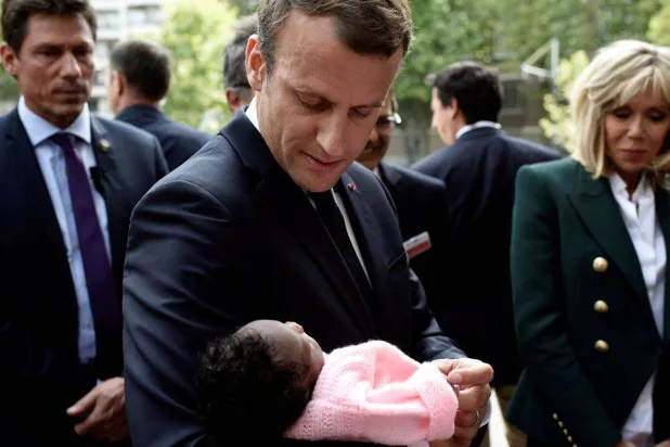 الرئيس الفرنسي إيمانويل ماكرون برفقة زوجته بريجيت يحمل رضيعة خلال زيارته لمستشفى روبرت ديبري للأطفال في باريس (رويترز)