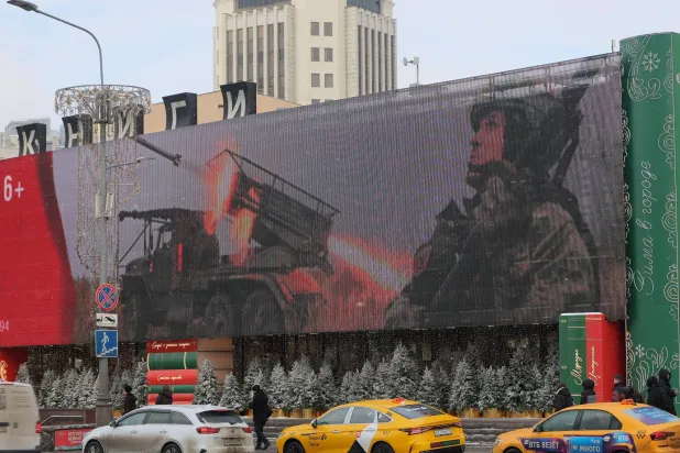 أشخاص يسيرون في أحد شوارع المدينة في موسكو بينما تعرض شاشة إلكترونية صورة جندي روسي (إ.ب.أ)