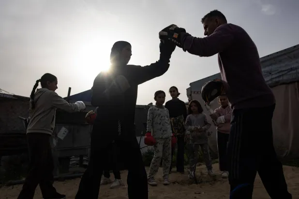 مدرب الملاكمة أسامة أيوب (يمين) يقوم بتدريب فتيات صغيرات داخل خيمة في منطقة المواصي بخان يونس جنوب قطاع غزة (إ.ب.أ)