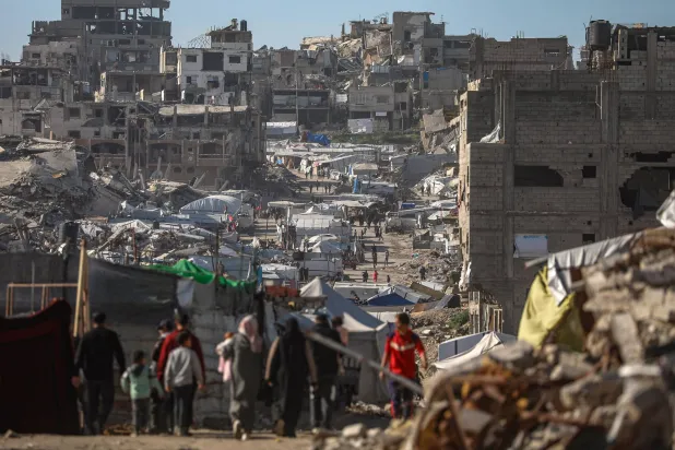 فلسطينيون نازحون داخلياً يسيرون بين أنقاض حي التفاح شرق مدينة غزة (إ.ب.أ)