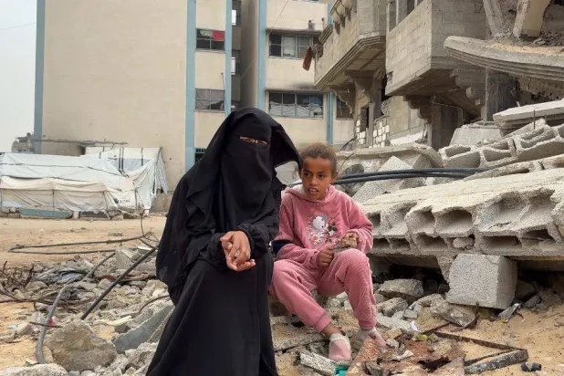 ضحى أبو سنيمة ووالدتها تجلسان بجوار منزل مهدم (الشرق الأوسط)