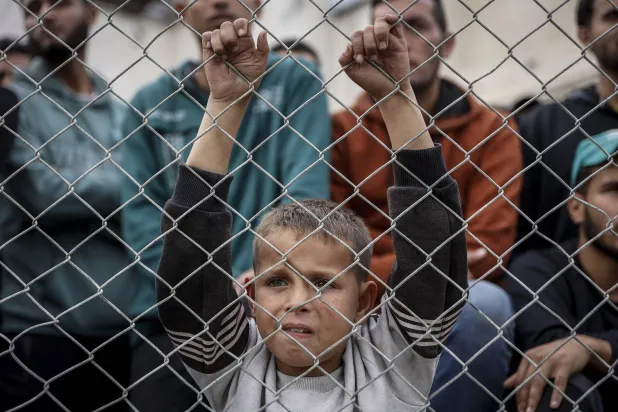 طفل فلسطيني يقف خلف سلك بلاستيكي وسط أنقاض المباني المدمرة في مدينة غزة (أ.ف.ب)