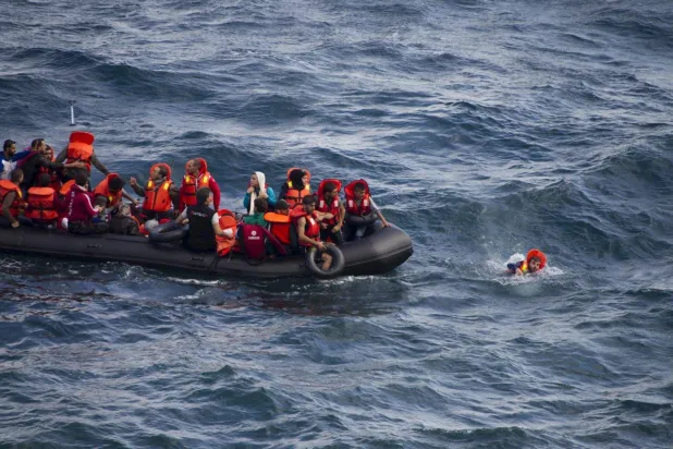 مهاجر يسبح بجوار قارب مطاطي مكتظ بالمهاجرين قرب شواطئ جزيرة ليسبوس اليونانية أثناء عبوره جزءاً من بحر إيجه من الساحل التركي (رويترز - أرشيفية)