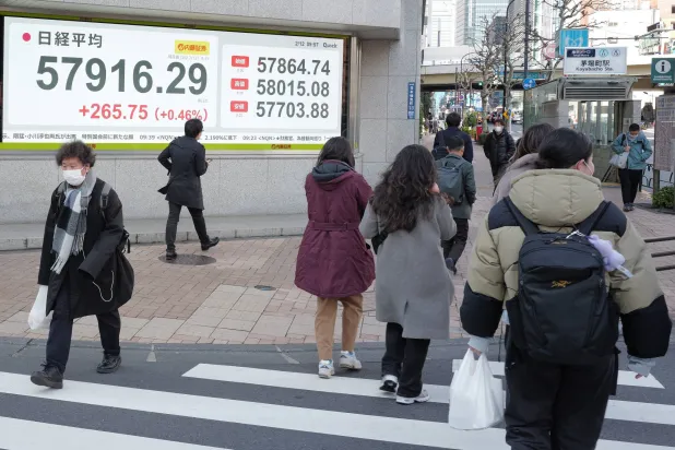 مشاة يعبرون الطريق أمام لوحة تعرض حركة الأسهم في وسط العاصمة اليابانية طوكيو (أ.ب)