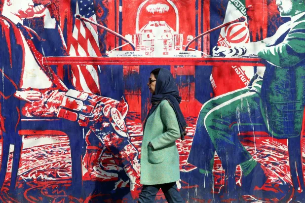 An Iranian woman walk past anti-US mural depicting Iran and US negotiation table, painted on the outer walls of the former US embassy, in Tehran on February 6, 2026. (AFP)