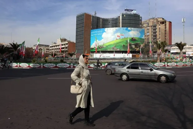 An Iranian woman walks past an anti-US billboard at Valiasr Square in Tehran, Iran, 14 February 2026, amid heightened regional tensions following an increased US military presence in the Middle East. (EPA)