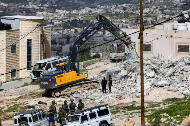 İsrail güvenlik güçleri tarafından kullanılan bir ekskavatör, işgal altındaki Batı Şeria’nın Beyt Gıva köyünde bir binayı yıkıyor. (AFP)