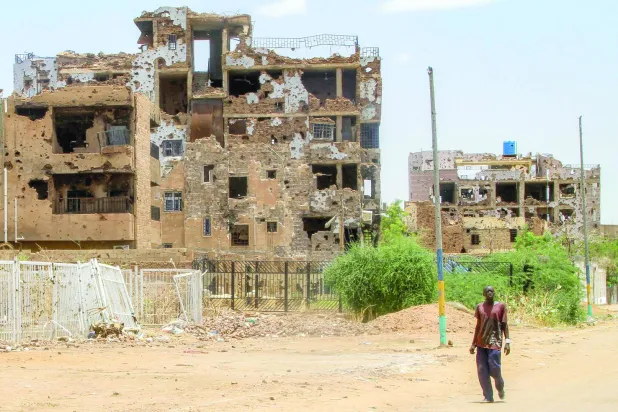 A man walks near heavily-damaged buildings in the Lamab suburb on the southwestern outskirts of Sudan's capital Khartoum on July 30, 2025 as residents return amidst reconstruction efforts. (Photo by Ebrahim Hamid / AFP)