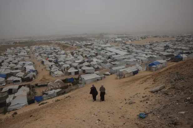 Women walk down a hill overlooking a camp for displaced Palestinians in Khan Younis, in the southern Gaza Strip, on February 14, 2026. (AFP)