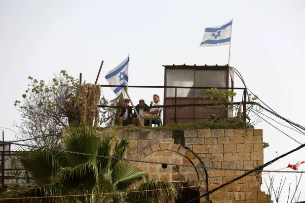  Israeli's sit on the roof next to a flag, as they monitor a weekly settlers' tour in Hebron, in the Israeli-occupied West Bank, February 14, 2026. (Reuters)